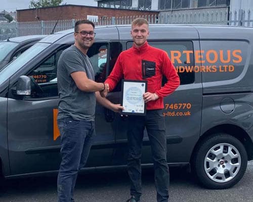 Evan and Ben smiling, hold a certificate in front of a Porteous van.